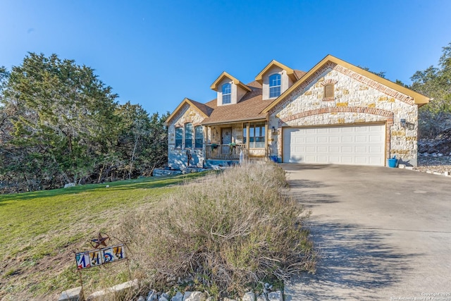 view of front of property with a porch, an attached garage, a front yard, stone siding, and driveway