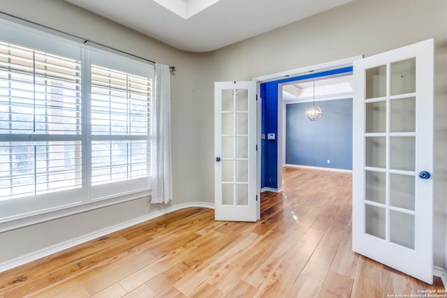 empty room featuring baseboards, french doors, wood finished floors, and a notable chandelier