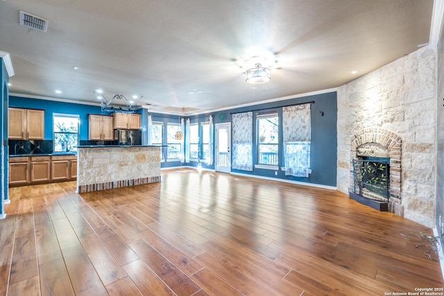 living room featuring light wood finished floors, a fireplace, visible vents, and crown molding