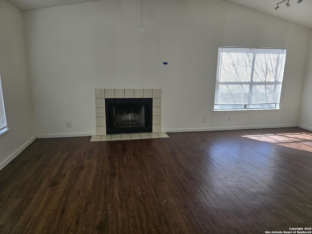 unfurnished living room featuring lofted ceiling, dark wood finished floors, a fireplace, and baseboards