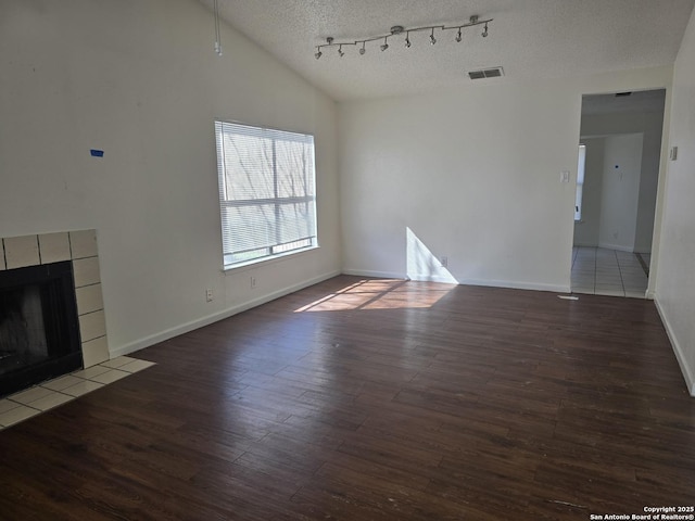 unfurnished living room with visible vents, dark wood-style flooring, vaulted ceiling, a textured ceiling, and a fireplace