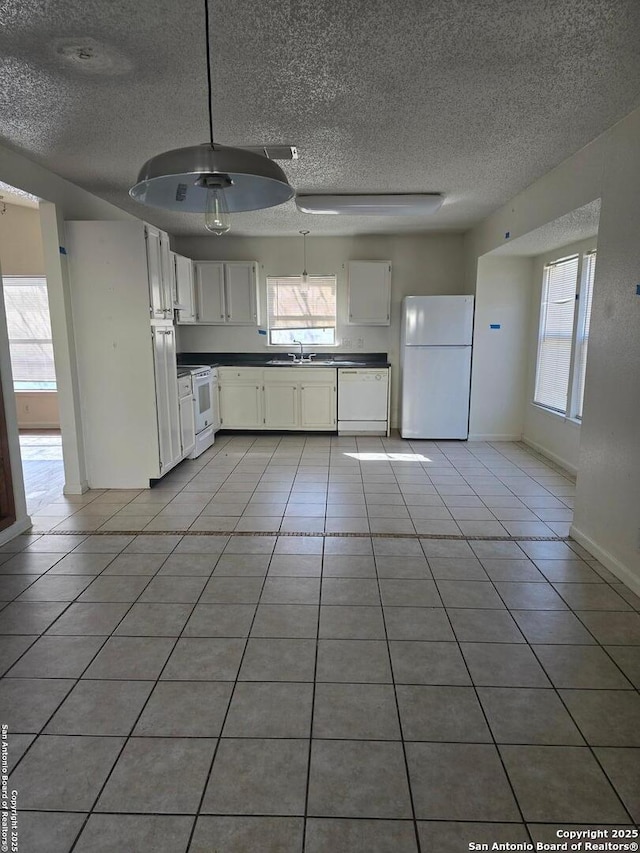 kitchen with white appliances, light tile patterned floors, white cabinets, dark countertops, and a sink