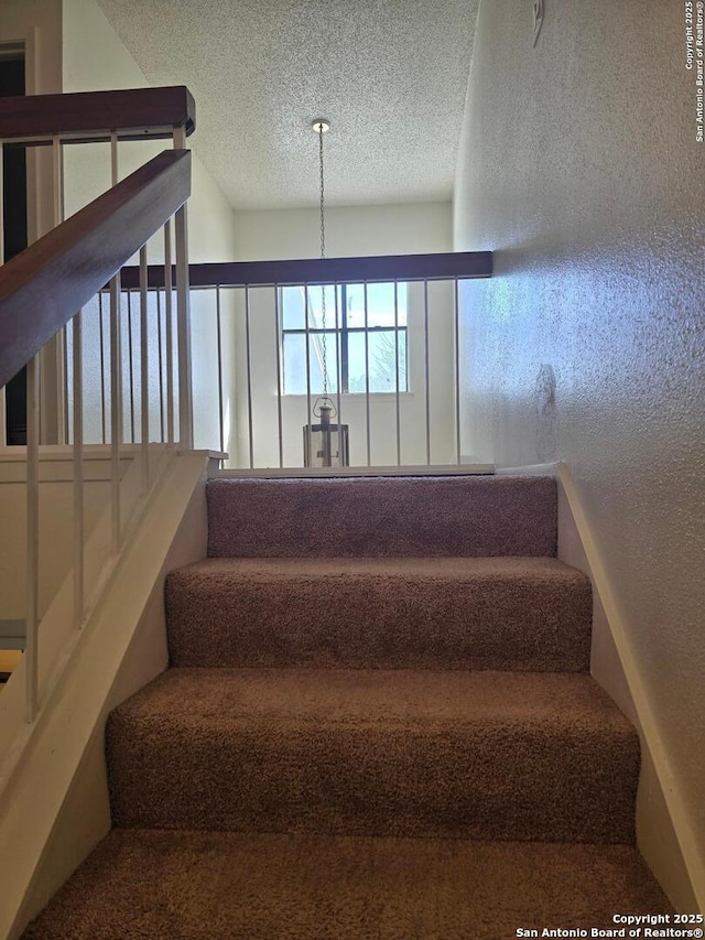 stairs with a textured ceiling and a textured wall