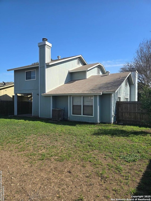 rear view of property featuring central air condition unit, fence, and a lawn