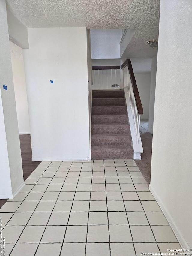 stairway with tile patterned flooring, baseboards, and a textured ceiling