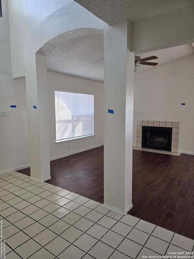 interior space featuring a textured ceiling, wood finished floors, a tile fireplace, and a ceiling fan