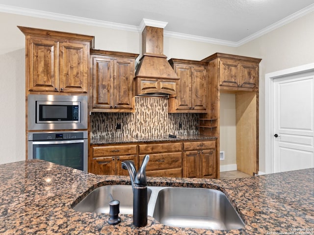 kitchen with custom exhaust hood, backsplash, appliances with stainless steel finishes, a sink, and dark stone countertops
