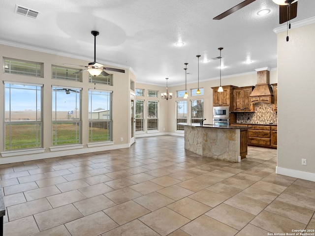 kitchen with stainless steel appliances, premium range hood, open floor plan, brown cabinetry, and decorative light fixtures
