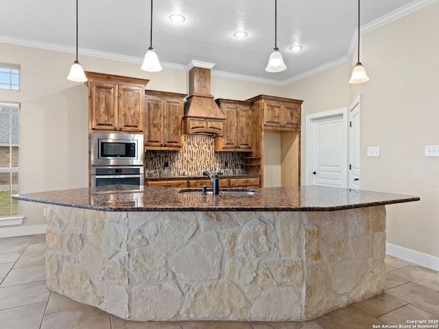 kitchen with decorative light fixtures, a center island with sink, appliances with stainless steel finishes, a sink, and premium range hood