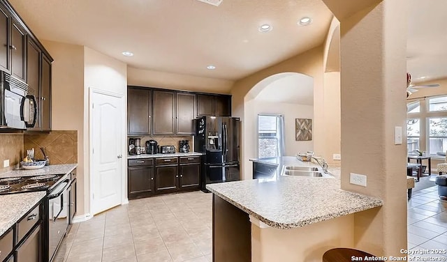 kitchen featuring a breakfast bar, a peninsula, dark brown cabinets, black appliances, and a sink