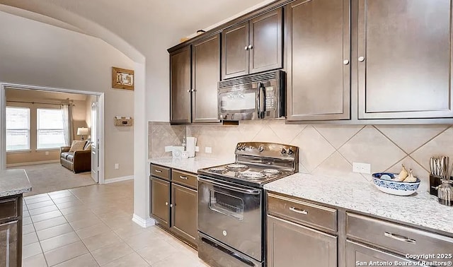 kitchen featuring dark brown cabinetry, arched walkways, decorative backsplash, light stone counters, and black appliances