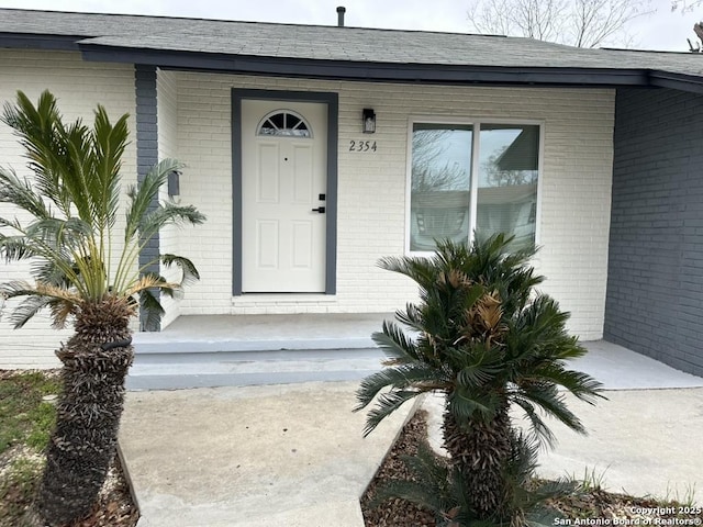 entrance to property featuring brick siding and a shingled roof