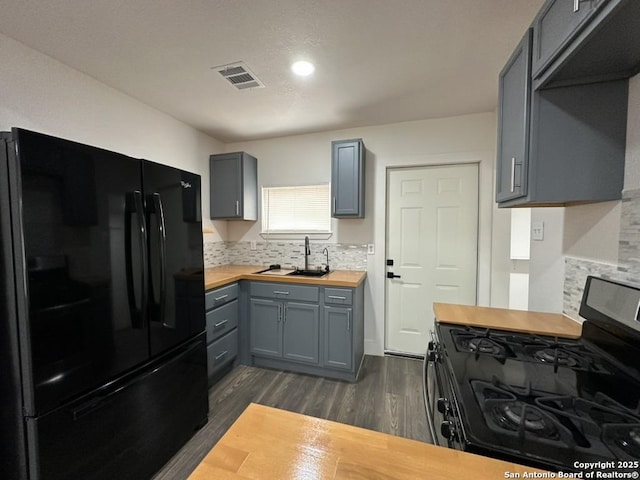 kitchen with stainless steel gas range oven, butcher block countertops, a sink, visible vents, and freestanding refrigerator