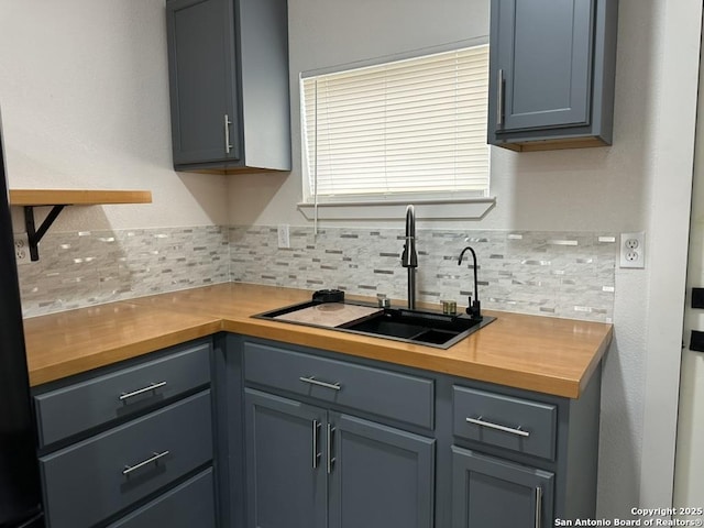 kitchen featuring gray cabinets, a sink, backsplash, and wooden counters