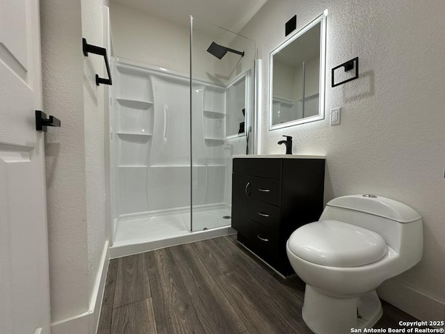 bathroom with a textured wall, toilet, wood finished floors, vanity, and a shower stall