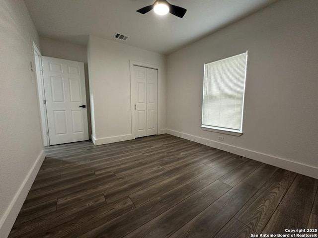 unfurnished bedroom with dark wood-type flooring, a closet, visible vents, and baseboards