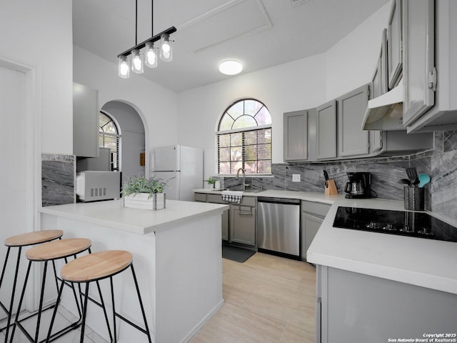 kitchen featuring freestanding refrigerator, light countertops, gray cabinetry, a kitchen bar, and stainless steel dishwasher