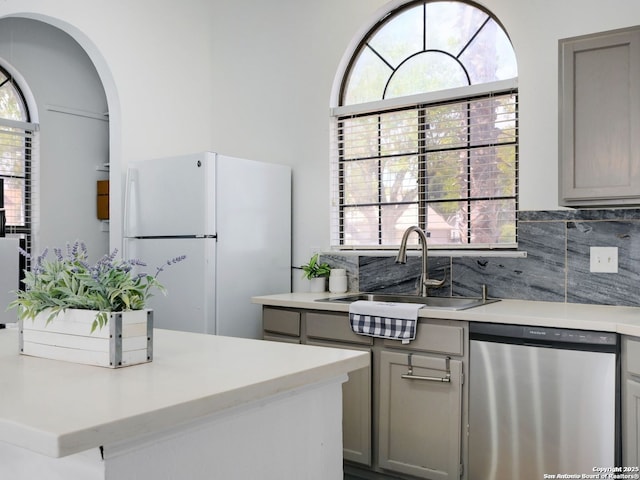 kitchen featuring a sink, light countertops, dishwasher, and freestanding refrigerator