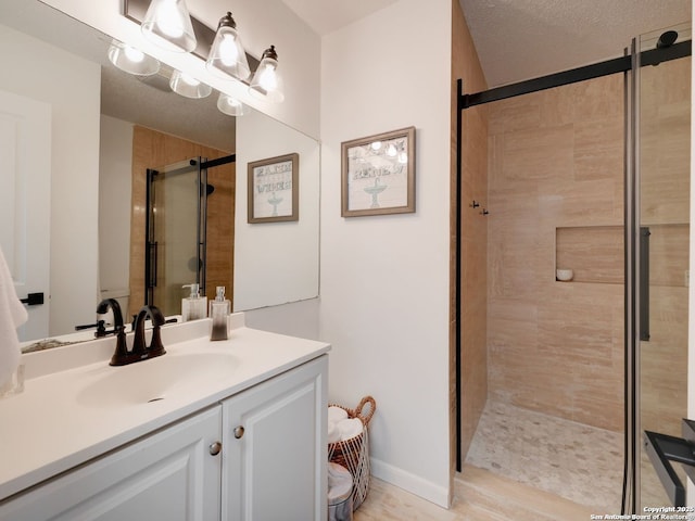 full bathroom featuring baseboards, a shower stall, vanity, and a textured ceiling