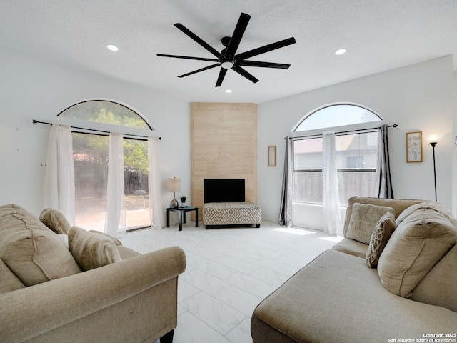 living area featuring a tile fireplace, marble finish floor, a healthy amount of sunlight, and a textured ceiling