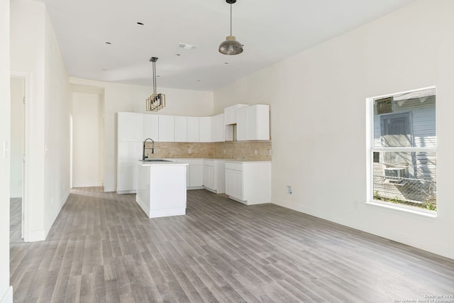 kitchen featuring tasteful backsplash, white cabinetry, a kitchen island, a sink, and light wood-type flooring