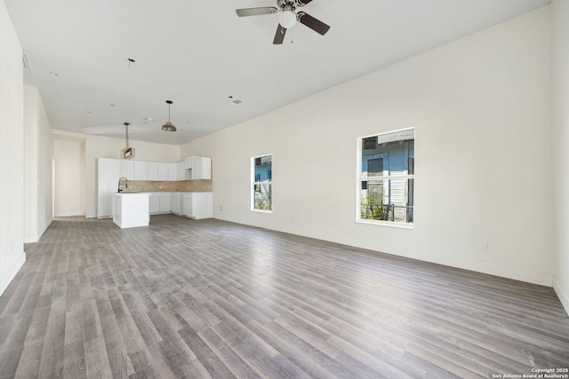 unfurnished living room featuring light wood finished floors, a sink, a ceiling fan, and baseboards