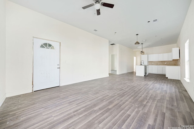 unfurnished living room featuring a ceiling fan, light wood-type flooring, visible vents, and a sink