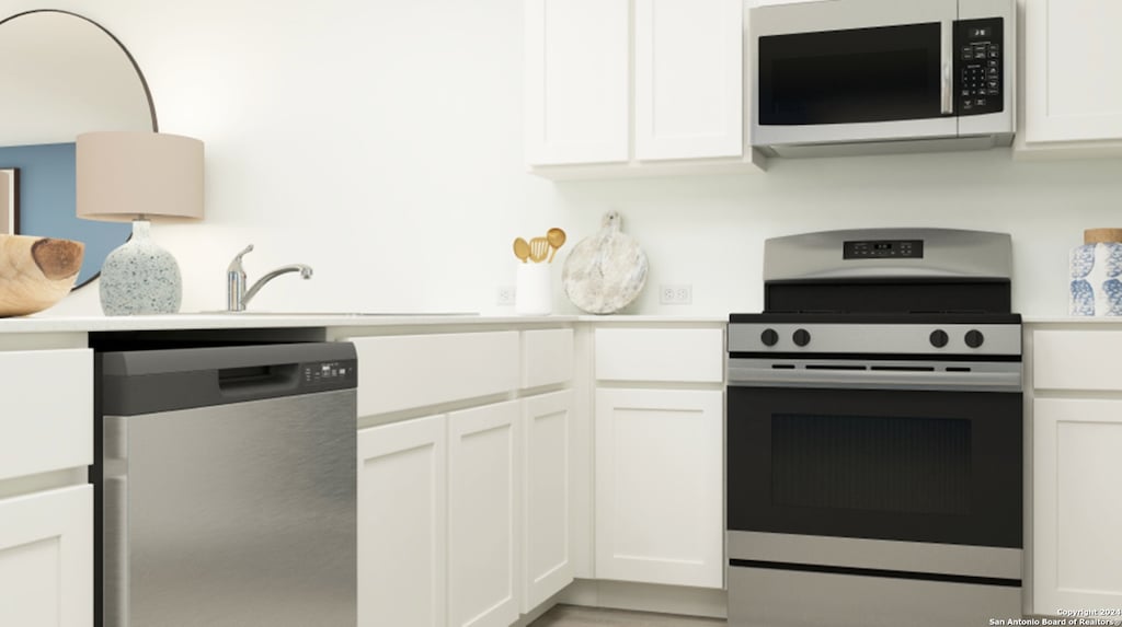 kitchen with stainless steel appliances, white cabinets, light countertops, and a sink