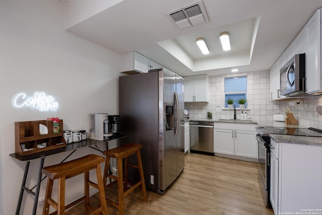 kitchen with a tray ceiling, stainless steel appliances, tasteful backsplash, visible vents, and white cabinetry