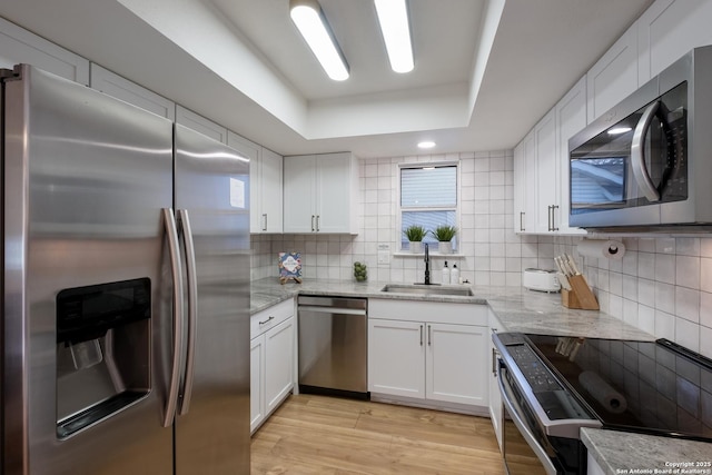 kitchen featuring white cabinets, stainless steel appliances, a sink, and a raised ceiling