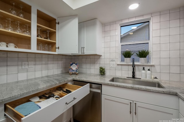 kitchen featuring backsplash, white cabinets, a sink, light stone countertops, and dishwasher