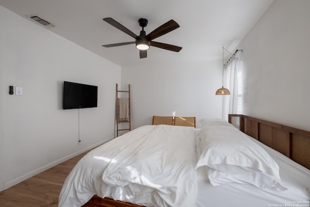 bedroom with a ceiling fan, wood finished floors, visible vents, and baseboards