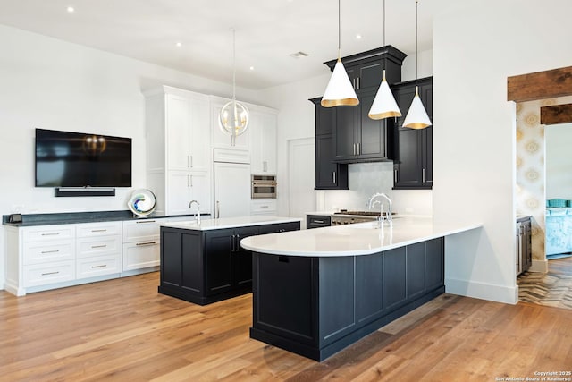 kitchen featuring a sink, stainless steel oven, an island with sink, light wood-type flooring, and paneled refrigerator