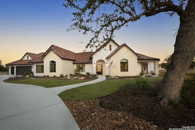 mediterranean / spanish-style home featuring concrete driveway, a tiled roof, an attached garage, a front yard, and stucco siding