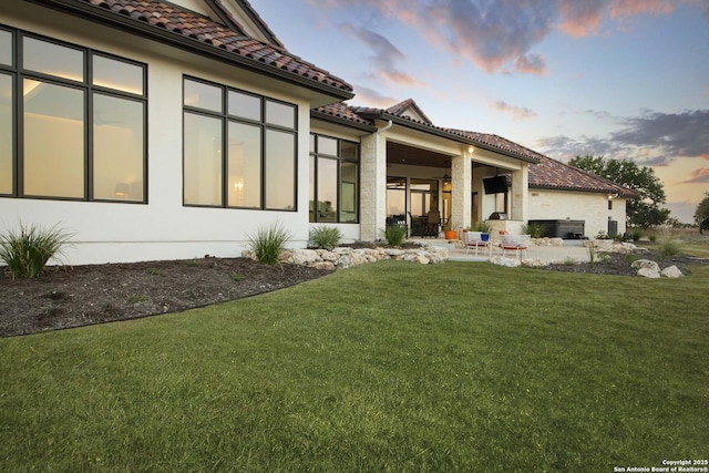 back of house with a tiled roof, a yard, a patio area, and stucco siding