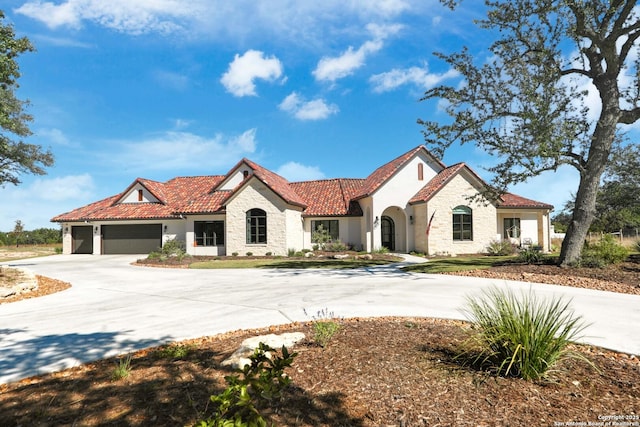 mediterranean / spanish house with stucco siding, an attached garage, stone siding, driveway, and a tiled roof