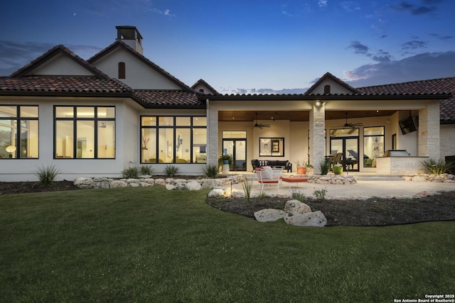 back of property featuring stucco siding, a lawn, a ceiling fan, a patio area, and a tiled roof