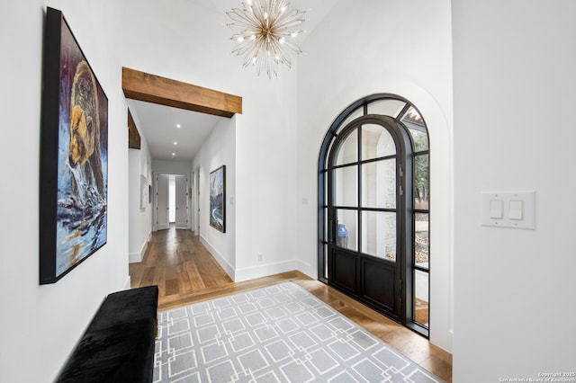 foyer entrance featuring a notable chandelier, recessed lighting, a towering ceiling, wood finished floors, and baseboards