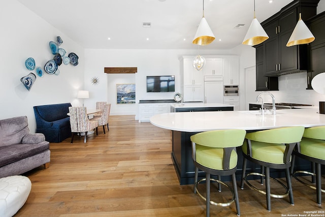 kitchen with light wood-type flooring, open floor plan, visible vents, and a center island with sink