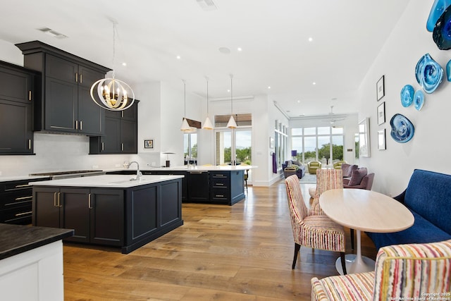 kitchen featuring visible vents, open floor plan, light wood finished floors, an island with sink, and cooktop