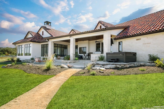 rear view of house featuring a tile roof, a patio area, a lawn, and a hot tub