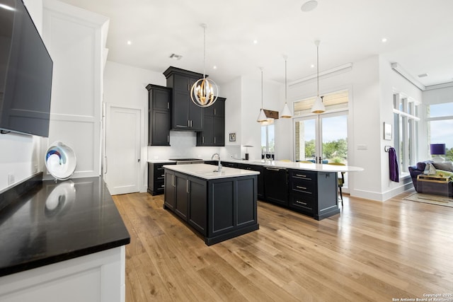 kitchen featuring light wood-style flooring, a kitchen island with sink, a sink, black dishwasher, and pendant lighting