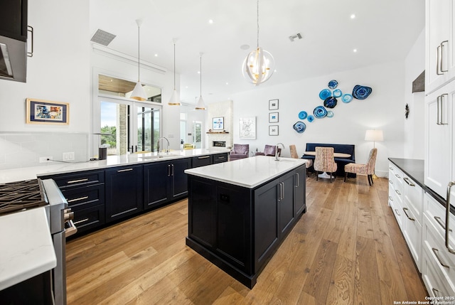 kitchen featuring visible vents, open floor plan, a sink, dark cabinets, and light wood-type flooring