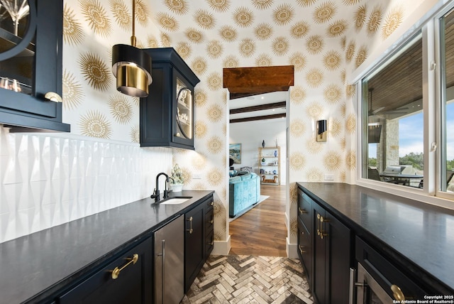 kitchen with dark countertops, wallpapered walls, glass insert cabinets, and a sink