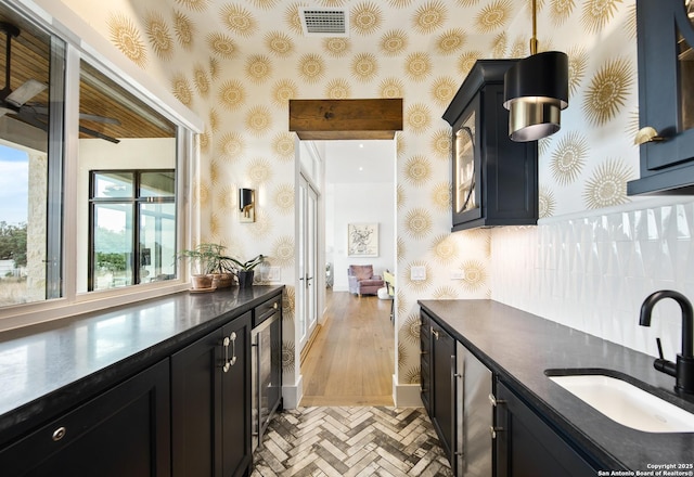 kitchen with dark countertops, visible vents, a sink, dark cabinetry, and wallpapered walls