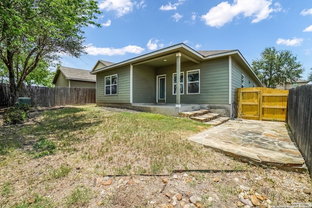 rear view of property featuring a patio, a lawn, fence, and a gate