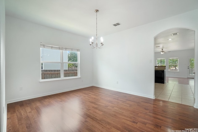 empty room featuring arched walkways, ceiling fan with notable chandelier, wood finished floors, visible vents, and baseboards