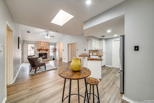 kitchen featuring a fireplace, light wood-style floors, open floor plan, white cabinetry, and a peninsula