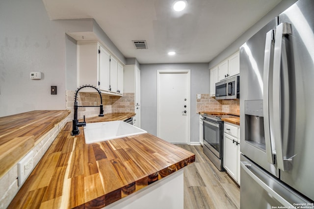 kitchen featuring butcher block countertops, appliances with stainless steel finishes, light wood-style floors, white cabinetry, and a sink