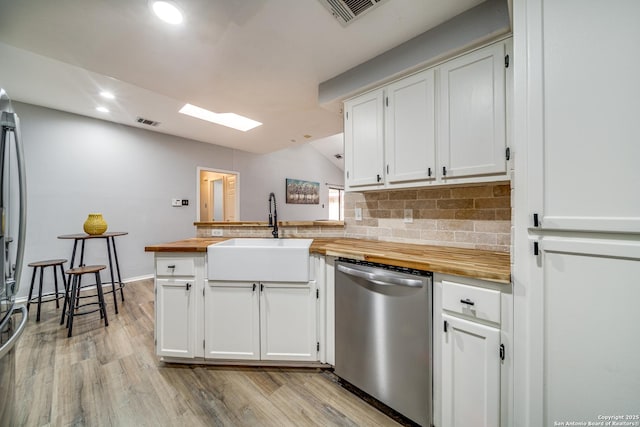 kitchen featuring stainless steel dishwasher, butcher block countertops, a sink, and white cabinets